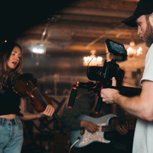 Filmmaker capturing a musician playing violin during an indoor music video shoot.