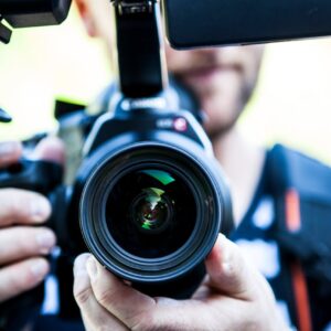 A close-up shot of a cameraman filming, focusing on the camera lens and equipment.