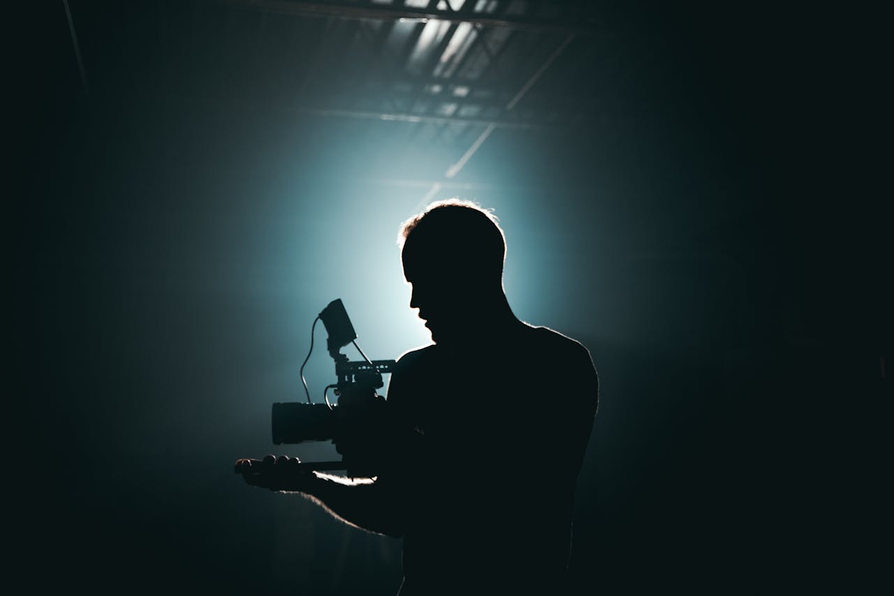 our-stories Silhouette of a cinematographer with camera gear in a dramatic, low light setting.