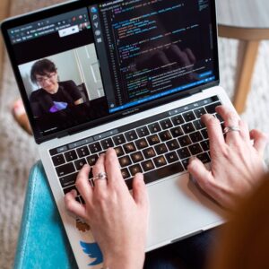 Person coding on a laptop during a video conference, showcasing remote work.