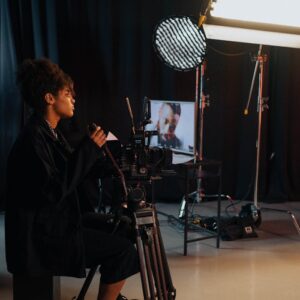 Videographer operating camera in a dark studio with lighting equipment and monitors.