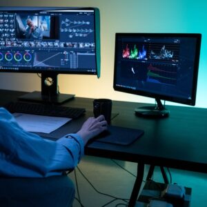 A video editor works on dual monitors in a modern setup, focusing on color grading and editing visuals.